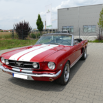 Roter Ford Mustang Cabrio mit weißen Rennstreifen, geparkt auf einem Firmenhof